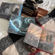 Three books with dragon and fantasy-themed illustrated endpapers on a checkered fabric surface with a typewriter and bottle.