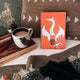 Nimona Illumicrate Exclusive foil hardcover displayed against a brown cushion, next to a mug of coffee.
